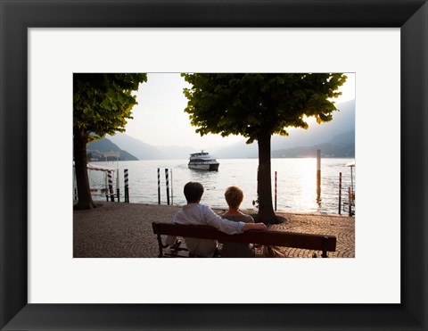 Framed Couple sitting on bench and watching ferry approaching dock along the Lake Como, Bellagio, Province of Como, Lombardy, Italy Print