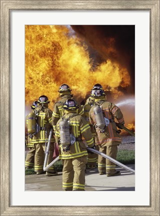 Framed Rear view of a group of firefighters extinguishing a fire vertical Print