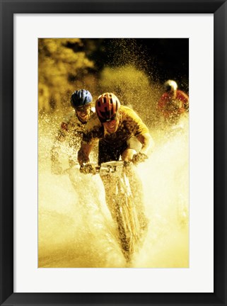 Framed Young men riding bicycles through water Print