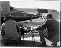 Framed Rear view of two men crouching near fighter planes, X-15 Rocket Research Airplane, B-52 Mothership