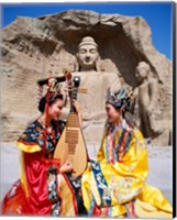 Framed Two girls in traditional costumes in front of the Buddha Statue, China