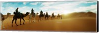 Framed Tourists riding camels through the Sahara Desert landscape led by a Berber man, Morocco