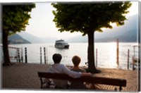 Framed Couple sitting on bench and watching ferry approaching dock along the Lake Como, Bellagio, Province of Como, Lombardy, Italy