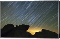 Framed Light pollution illuminates the sky and star tails above large boulders