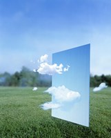 Framed White clouds passing through a pale blue horizontal of sky with green grass, trees and sky in the distance
