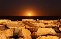 Framed moon rising behind rocks lit by a nearby fire in Miramar, Argentina