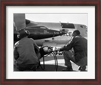 Framed Rear view of two men crouching near fighter planes, X-15 Rocket Research Airplane, B-52 Mothership