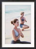 Framed Young woman and a mid adult woman meditating on the beach