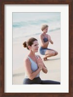 Framed Young woman and a mid adult woman meditating on the beach