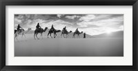 Framed Tourists riding camels through the Sahara Desert landscape led by a Berber man, Morocco (black and white)