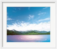 Framed Pink light cast down on two rings in lavender water with deep blue sky and clouds over green mountains in distance