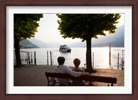 Framed Couple sitting on bench and watching ferry approaching dock along the Lake Como, Bellagio, Province of Como, Lombardy, Italy