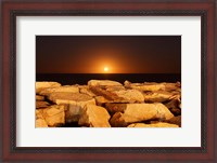 Framed moon rising behind rocks lit by a nearby fire in Miramar, Argentina