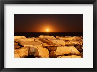 Framed moon rising behind rocks lit by a nearby fire in Miramar, Argentina