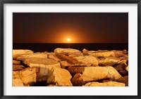 Framed moon rising behind rocks lit by a nearby fire in Miramar, Argentina