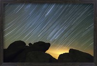 Framed Light pollution illuminates the sky and star tails above large boulders