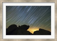 Framed Light pollution illuminates the sky and star tails above large boulders