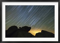 Framed Light pollution illuminates the sky and star tails above large boulders