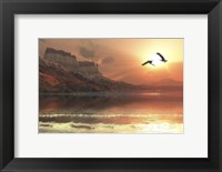 Framed Two Bald Eagles fly along a mountainous coastline at sunset